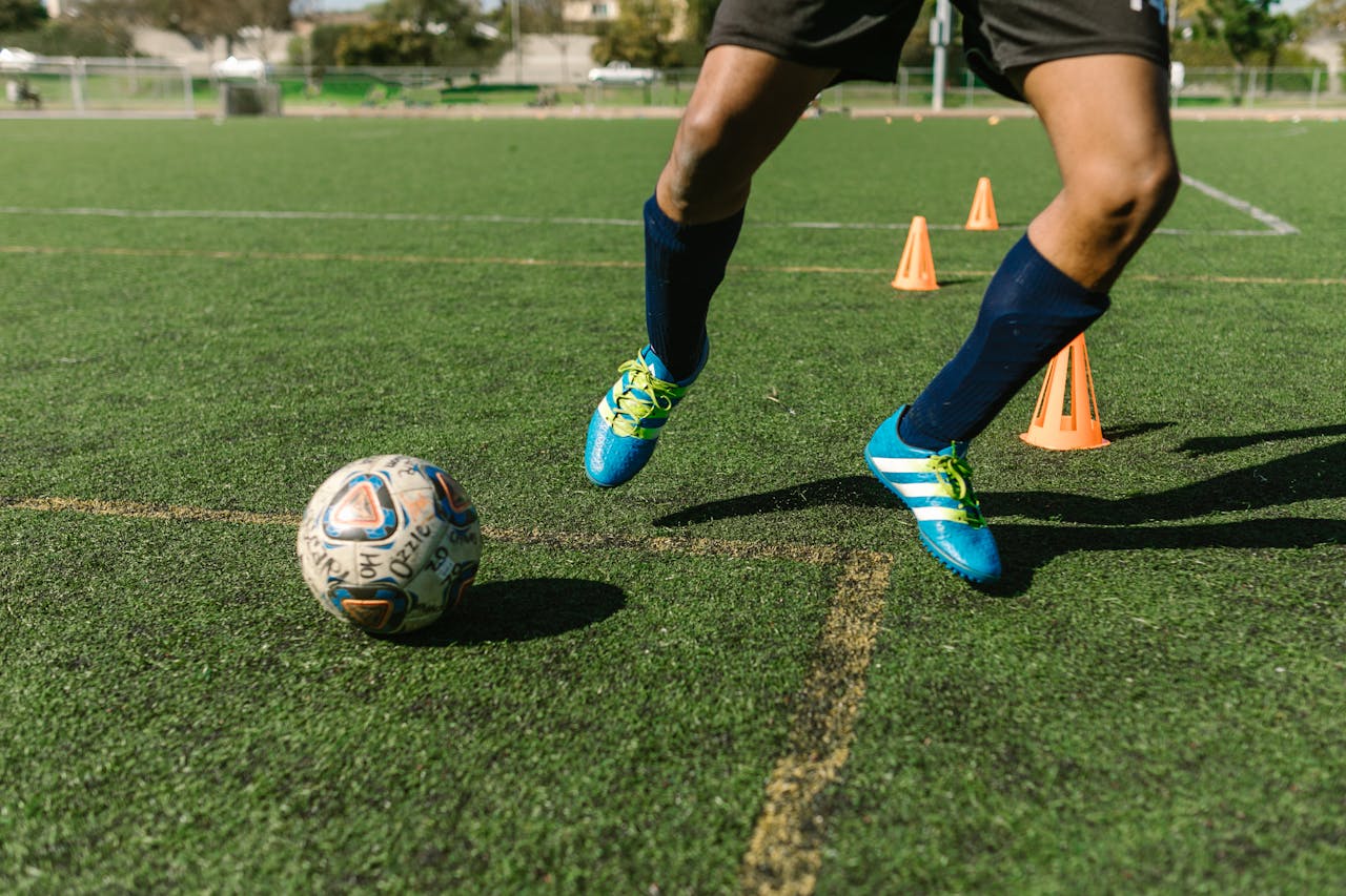 Dynamic image of a soccer player practicing drills on a grass field with vibrant shoes and cones.